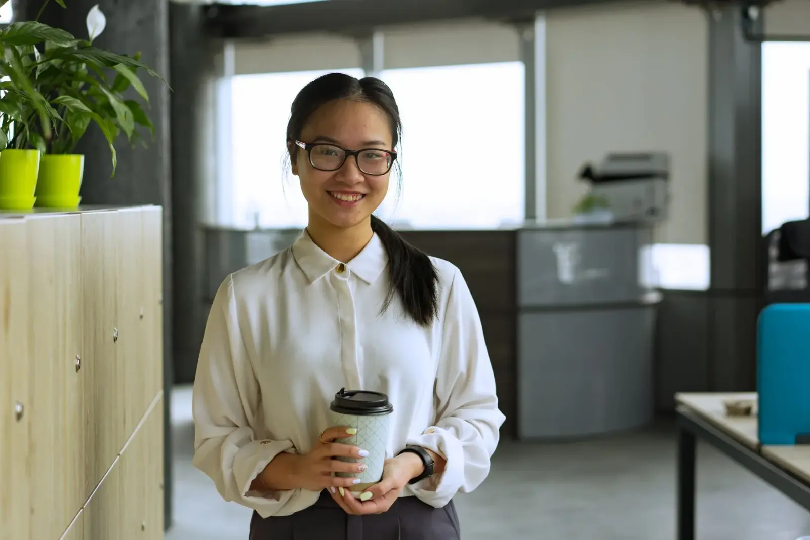 Người phụ nữ đeo kính cầm cốc cà phê, mỉm cười